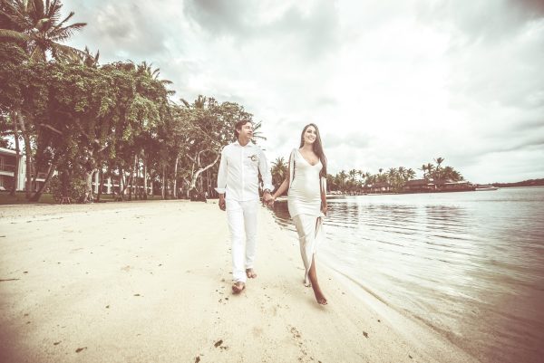 A couple is holding hands while they walk on the beach 