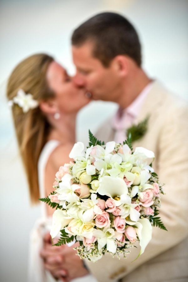 groom and bride kissing at the back of rose bouquet
