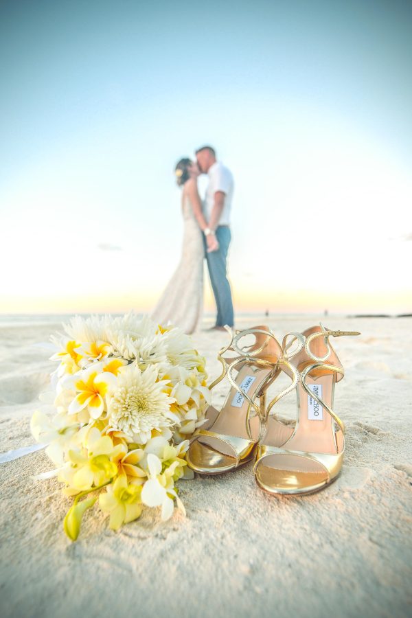 couple kissing on the beach in front of flower and shoes