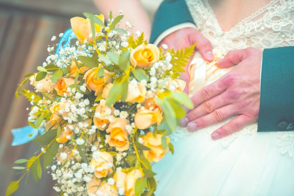 creative shot of groom forming a heart with hands with yellow bouquet