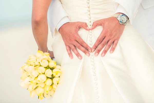 creative shot of groom forming a heart with hands with yellow flowers