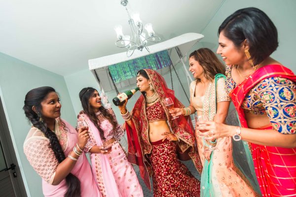 Bride drinking champagne with bridesmaids looking at her 