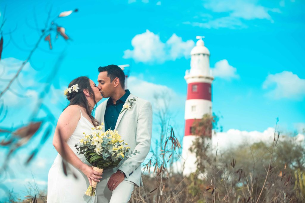 Couple kissing while the lady holds a bouquet with the lighthouse in the background